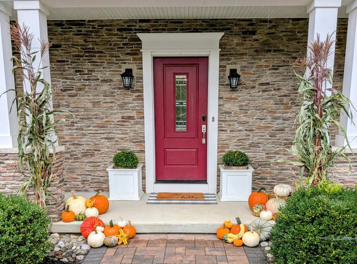 Fall porch display with pumpkins and cornstalks around a red door and stone facade