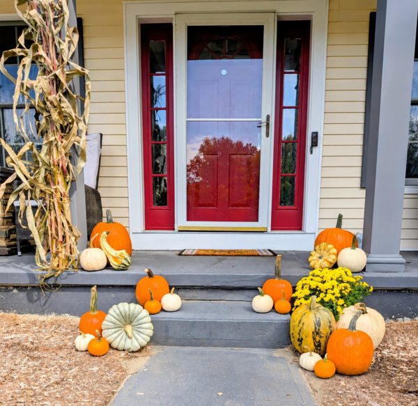 Fall pumpkins, mums and cornstalks arranged at a red-door porch