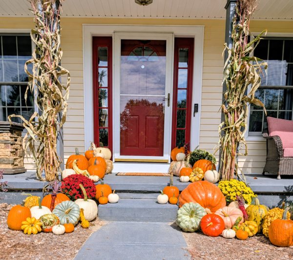 Fall pumpkins, mums and cornstalks arranged at a red-door porch