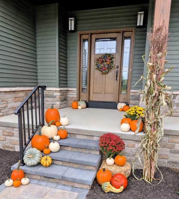 Fall pumpkins, mums and cornstalks arranged at a green porch and stone steps