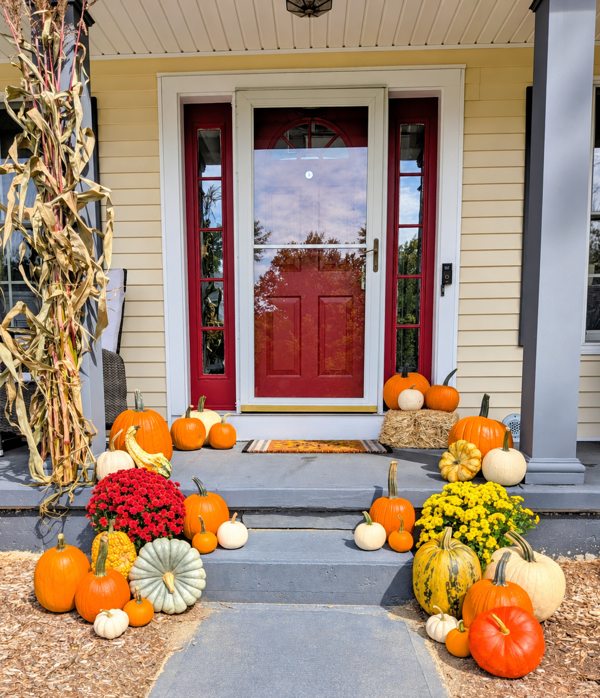 Fall pumpkins, mums and cornstalks arranged at a red-door porch