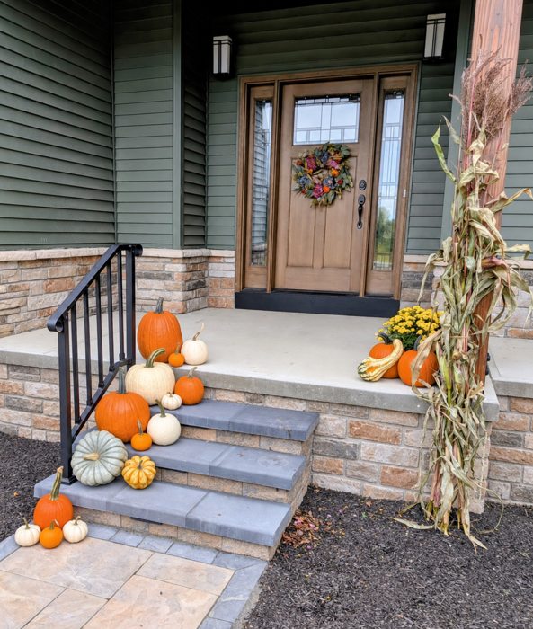 Fall pumpkins, mums and cornstalks arranged at a green porch and stone steps